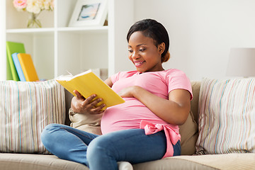 Image showing happy pregnant african woman reading book at home