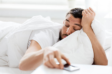 Image showing young man reaching for smartphone in bed