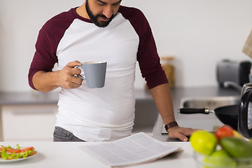 Image showing man with coffee reading newspaper at home kitchen