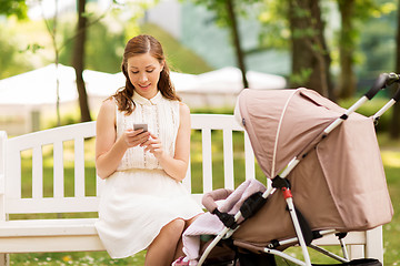 Image showing happy mother with smartphone and stroller at park