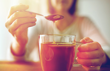 Image showing close up of woman adding honey to tea with lemon