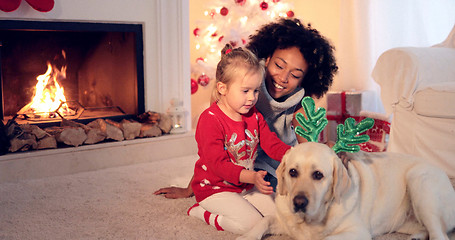 Image showing Mom and daughter in sweaters play with pet dog