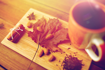 Image showing cup of tea, maple leaf and almond on wooden board