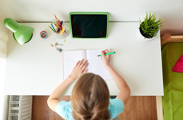Image showing girl with tablet pc writing to notebook at home