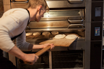 Image showing baker putting dough into bread oven at bakery