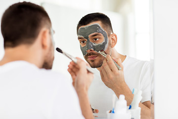 Image showing young man applying clay mask to face at bathroom