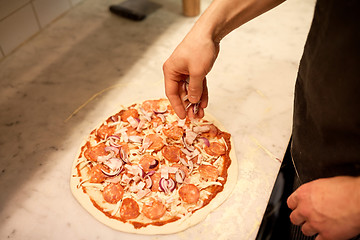 Image showing cook adding onion to salami pizza at pizzeria