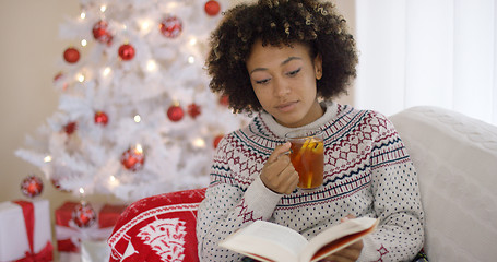 Image showing Woman reading a book in front of a Christmas tree