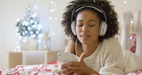 Image showing Lady in white sweater on bed listening to music