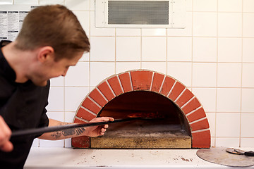 Image showing man with peel placing pizza to oven at pizzeria