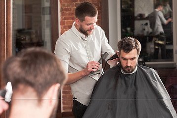 Image showing Young handsome barber making haircut of attractive man in barbershop