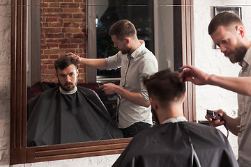 Image showing Young handsome barber making haircut of attractive man in barbershop