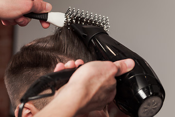 Image showing The hands of barber making haircut to young man in barbershop