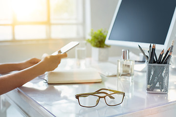 Image showing Close-up of female hands using smart phone while working on computer at modern office interior