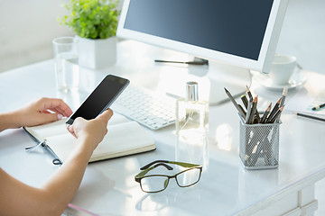 Image showing Close-up of female hands using smart phone while working on computer at modern office interior