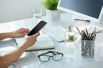 Image showing Close-up of female hands using smart phone while working on computer at modern office interior