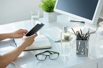 Image showing Close-up of female hands using smart phone while working on computer at modern office interior