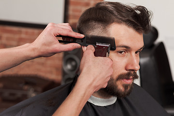 Image showing The hands of barber making haircut to young man in barbershop