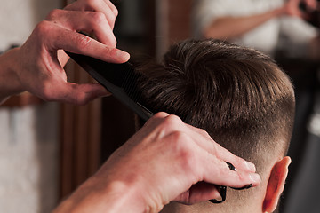 Image showing The hands of barber making haircut to young man in barbershop