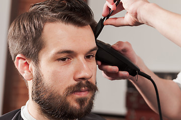 Image showing The hands of barber making haircut to young man in barbershop