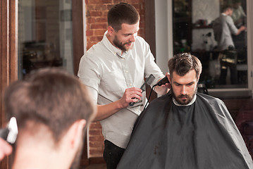 Image showing Young handsome barber making haircut of attractive man in barbershop