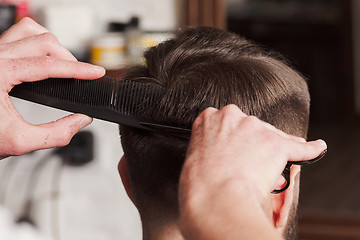 Image showing The hands of barber making haircut to young man in barbershop