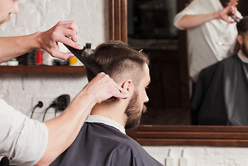 Image showing The hands of barber making haircut to young man in barbershop
