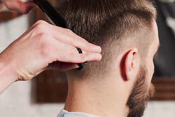 Image showing The hands of barber making haircut to young man in barbershop