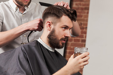 Image showing Young handsome barber making haircut of attractive man in barbershop