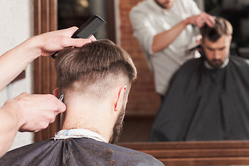 Image showing The hands of barber making haircut to young man in barbershop