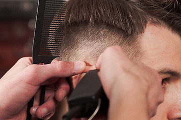 Image showing The hands of barber making haircut to young man in barbershop