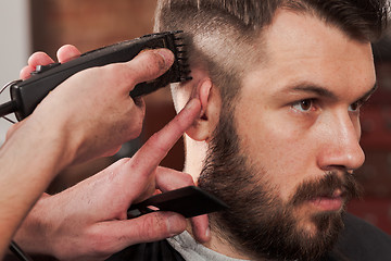 Image showing The hands of barber making haircut to young man in barbershop