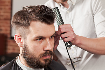 Image showing The hands of barber making haircut to young man in barbershop