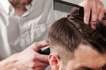 Image showing The hands of barber making haircut to young man in barbershop