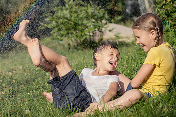 Image showing Happy kids sitting on the grass and pouring water from a hose.