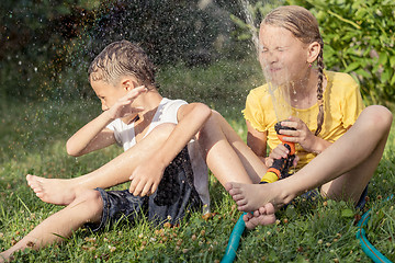Image showing Happy kids sitting on the grass and pouring water from a hose.
