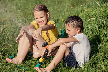 Image showing Happy kids sitting on the grass and pouring water from a hose.