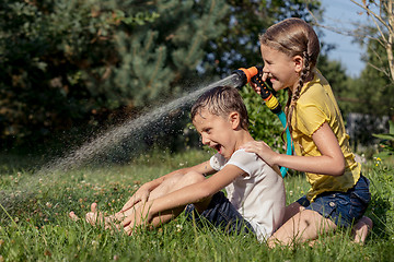 Image showing Happy kids sitting on the grass and pouring water from a hose.