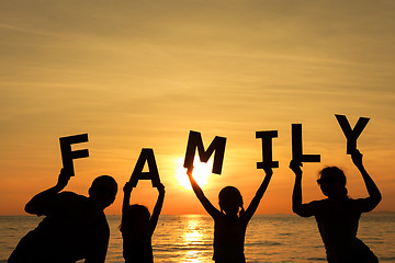 Image showing Happy family standing on the beach at the sunset time.