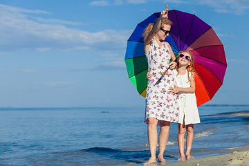 Image showing Mother and daughter playing with umbrella on the beach at the da