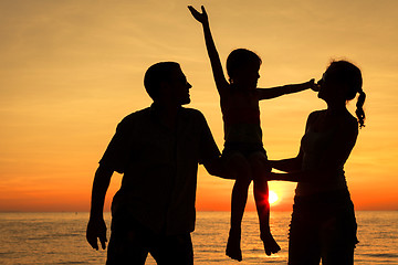 Image showing Happy family standing on the beach at the sunset time.