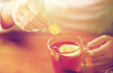 Image showing close up of woman adding ginger to tea with lemon