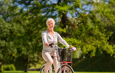 Image showing happy senior woman riding bicycle at summer park