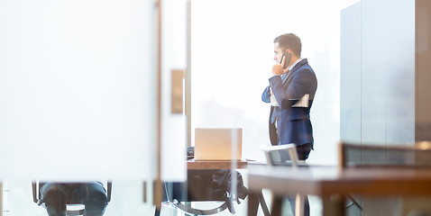 Image showing Businessman talking on a mobile phone while looking through window.