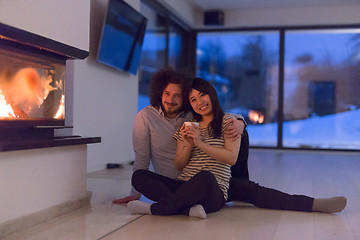 Image showing happy multiethnic couple sitting in front of fireplace