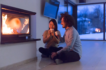 Image showing happy multiethnic couple sitting in front of fireplace