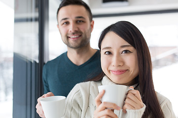 Image showing multiethnic couple enjoying morning coffee by the window