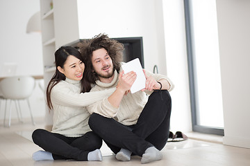 Image showing multiethnic couple using tablet computer in front of fireplace