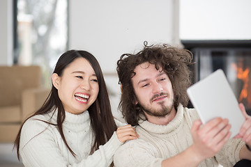 Image showing multiethnic couple using tablet computer in front of fireplace