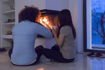 Image showing happy multiethnic couple sitting in front of fireplace